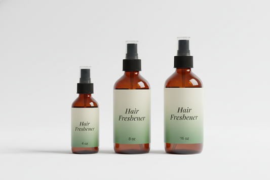 Generate a high-quality studio image with three amber spray bottles (4 oz, 8 oz, 16 oz). Each bottle must use a sleek black fine mist sprayer. The label text must be printed exactly as ‘Hair Freshener’ with the exact size written at the bottom as ‘4 oz,’ ‘8 oz,’ and ‘16 oz.’ Make sure the text is centered, sharp, and readable. Use a green-to-cream gradient label with a luxury minimal design and a white background.