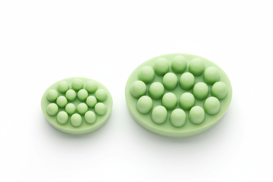 Generate a side-by-side image of two light green oval shampoo bars with exactly 13 rounded nubs on top. One bar should be 2.5 oz (smaller) and the other 5 oz (larger). No lettering or engraving on either bar. Clean studio background with soft shadows