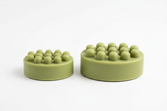 Generate a side-by-side image of two matcha-green oval detox shampoo bars with exactly 13 rounded nubs on top. One bar should be 2.5 oz (smaller) and the other 5 oz (larger). No lettering or engraving on either bar. Clean studio background with soft shadows